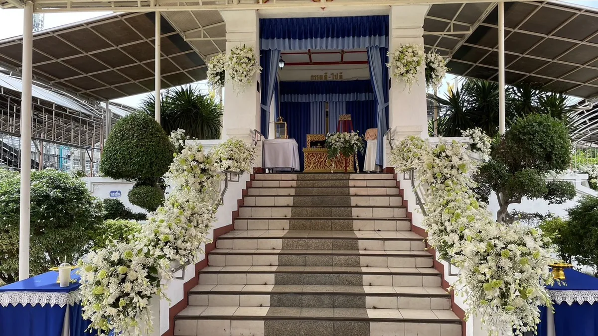 พวงหรีดดอกไม้สดโทนขาวตั้งเรียงหน้าสถานที่จัดพิธี พร้อมป้ายชื่อผู้ส่งที่อ่านได้ชัด